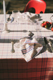 Table setting with a checkered napkin, and cutlery on a matching checkered tablecloth.