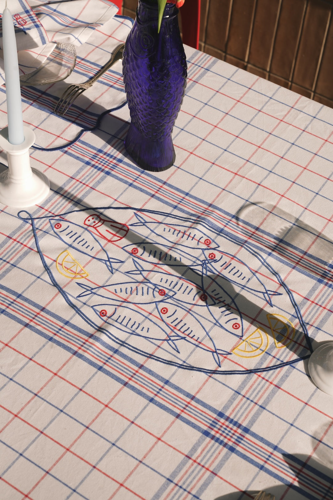 Fish-themed embroidery  on a checkered tablecloth with a blue vase in the background.