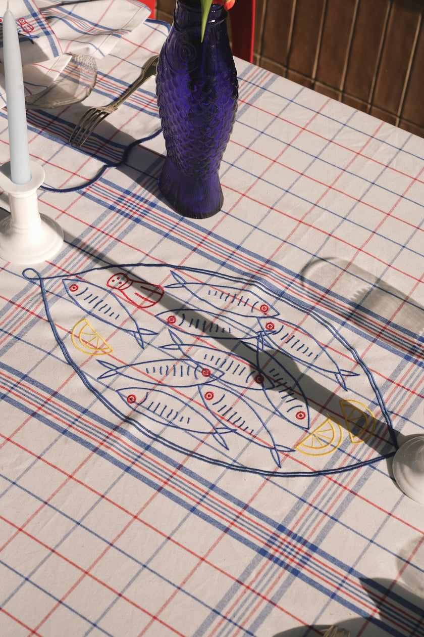 Fish-themed embroidery  on a checkered tablecloth with a blue vase in the background.