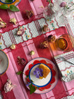 Decorative table setting with a pink tablecloth, floral plates, and a glass.