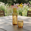 Amber glass carafe and glass on a wooden table in a garden 