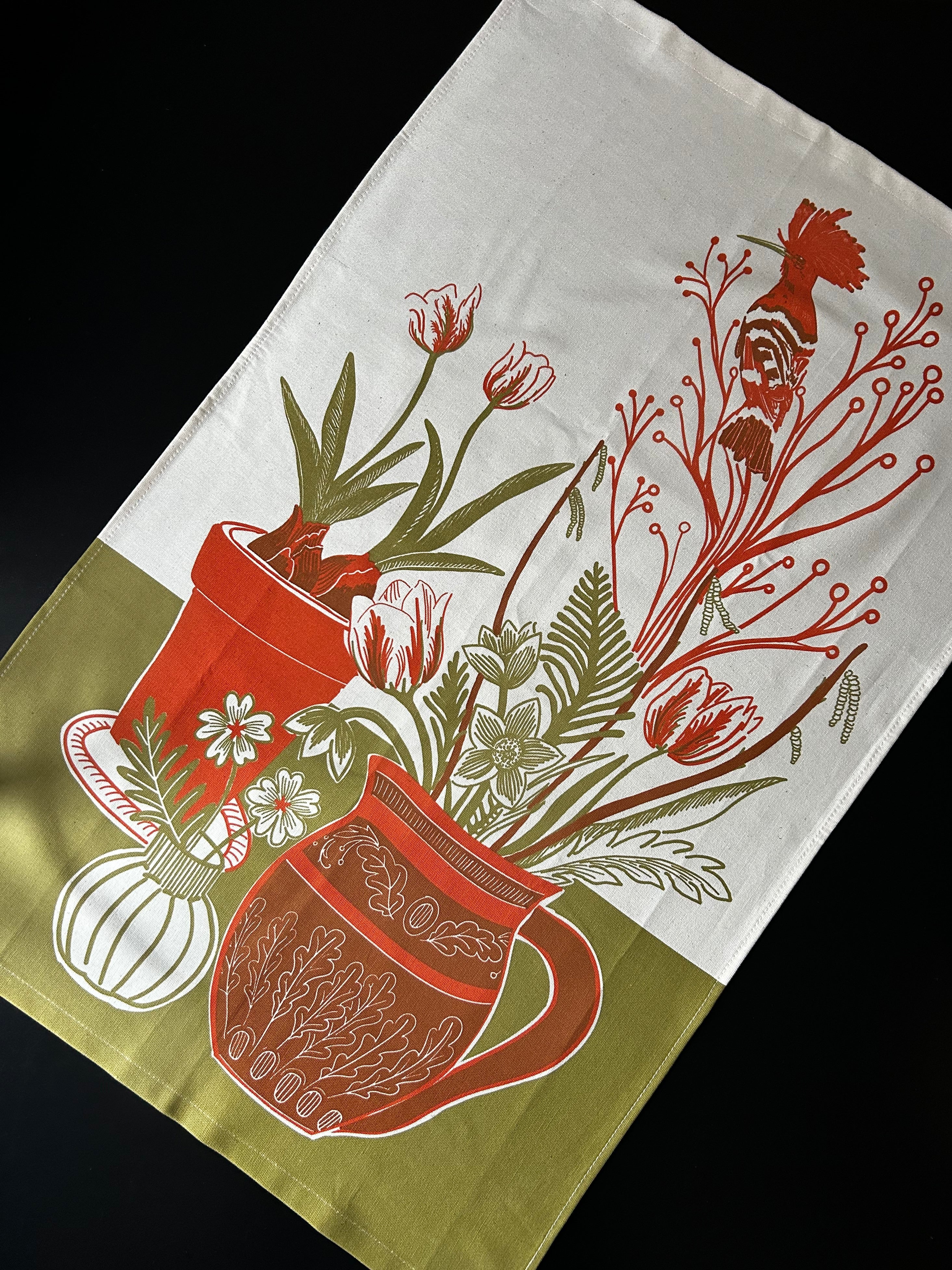 Decorative tea towel with bird, floral and pot design on a white background