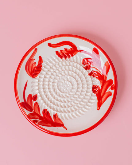 Round white plate with red floral patterns on a pink background