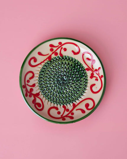 Decorative grater plate with red and green patterns on a pink background