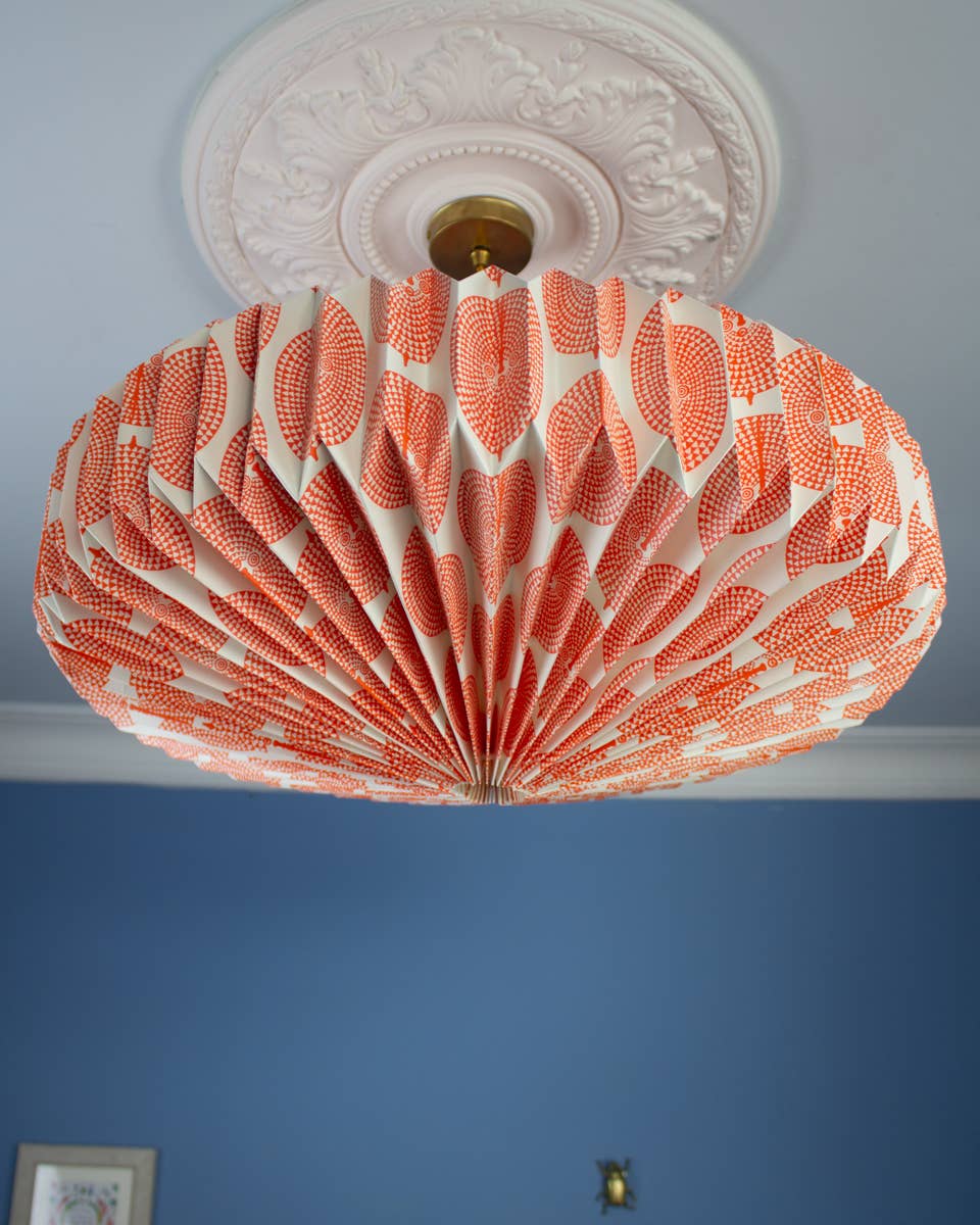 Orange and white decorative paper ceiling lightshade  on a blue wall.
