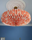 Orange and white decorative paper ceiling lightshade  on a blue wall.