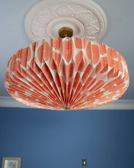 Orange and white decorative paper ceiling lightshade  on a blue wall.