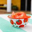 Small bowl with tomato pattern filled with sliced tomatoes on a green surface.