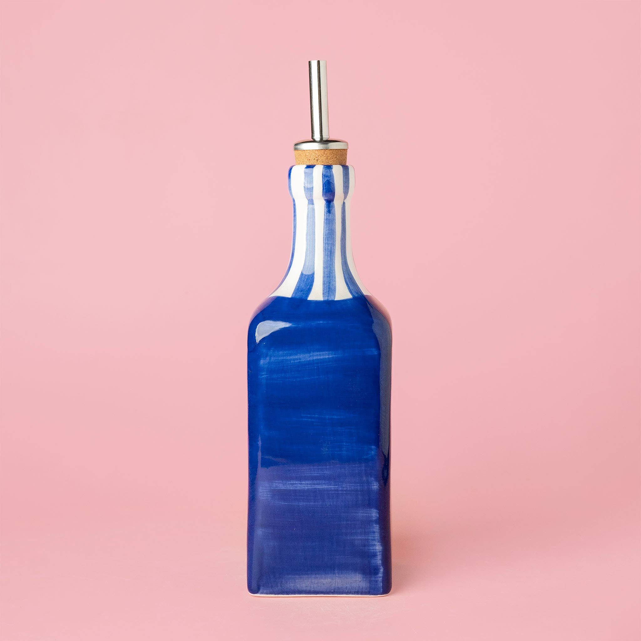 Blue ceramic oil pourer with striped pattern on a pink background