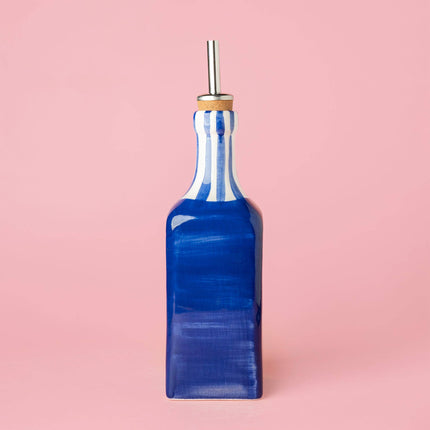 Blue ceramic oil pourer with striped pattern on a pink background