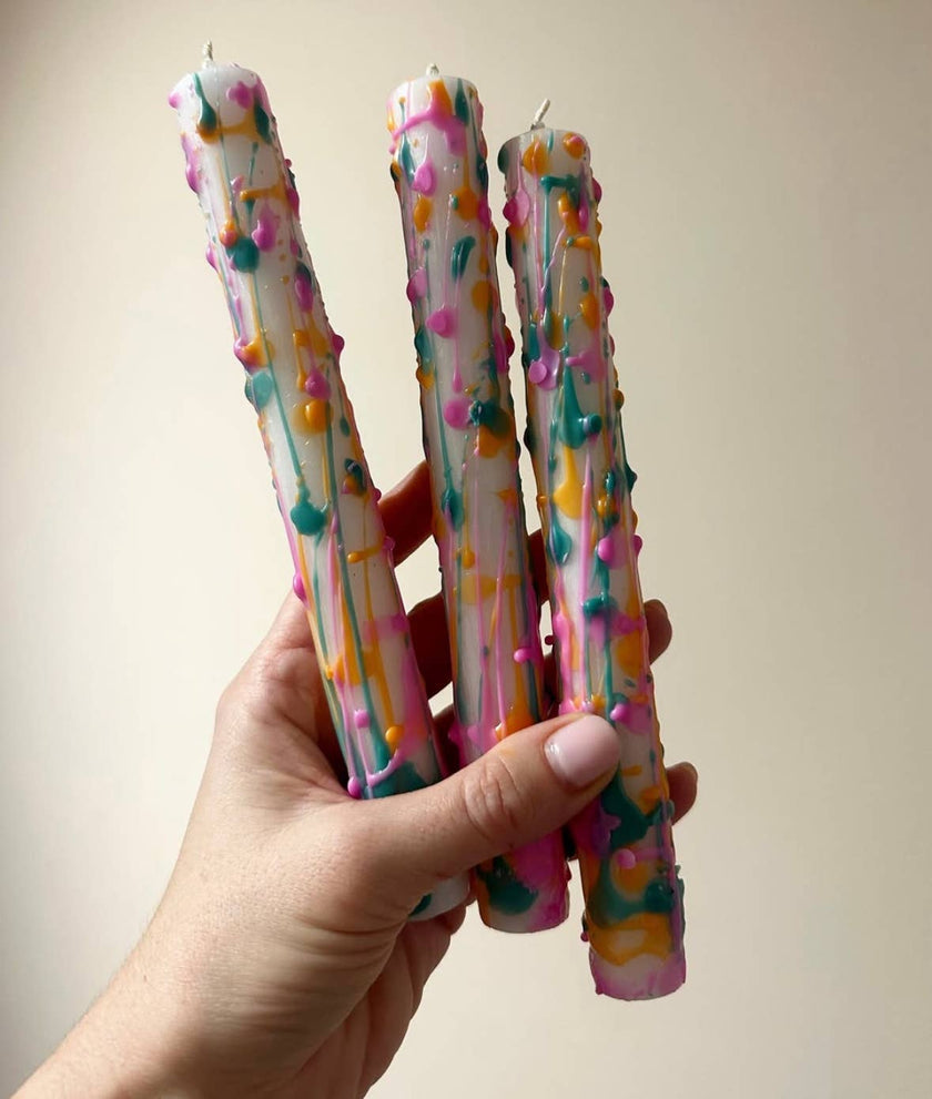 Hand holding three colorful decorated candles against a plain background