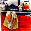 Red stove with a patterned towel hanging on the handle, books stacked to the left, and a kettle on top.