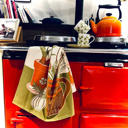 Red stove with a patterned towel hanging on the handle, books stacked to the left, and a kettle on top.