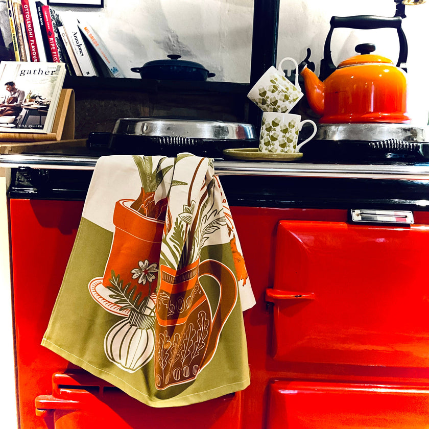 Red stove with a patterned towel hanging on the handle, books stacked to the left, and a kettle on top.