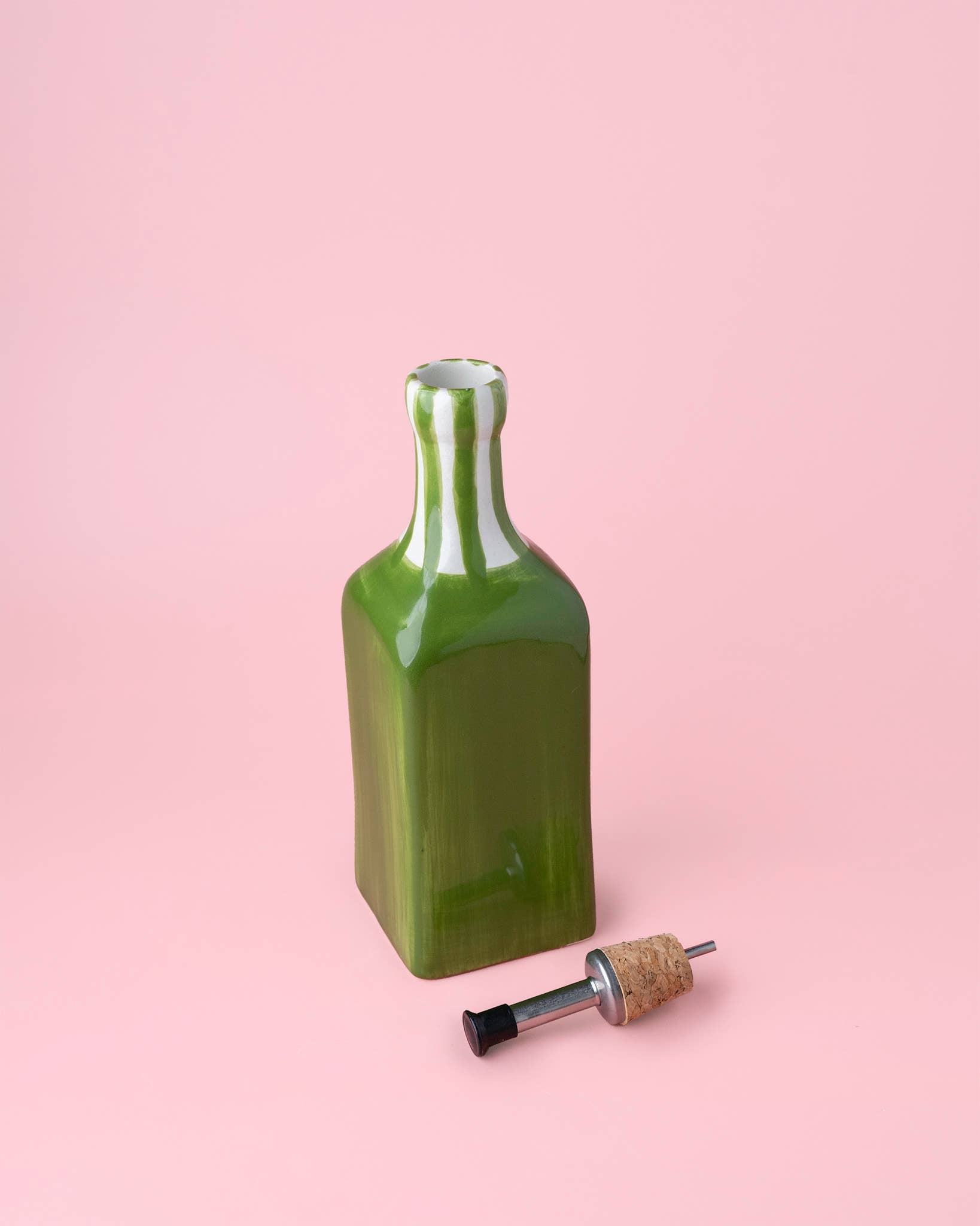 Green ceramic oil pourer with cork stopper on a pink background