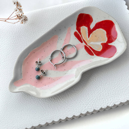 Jewellery dish with a red flower design holding earrings and a ring on a white background