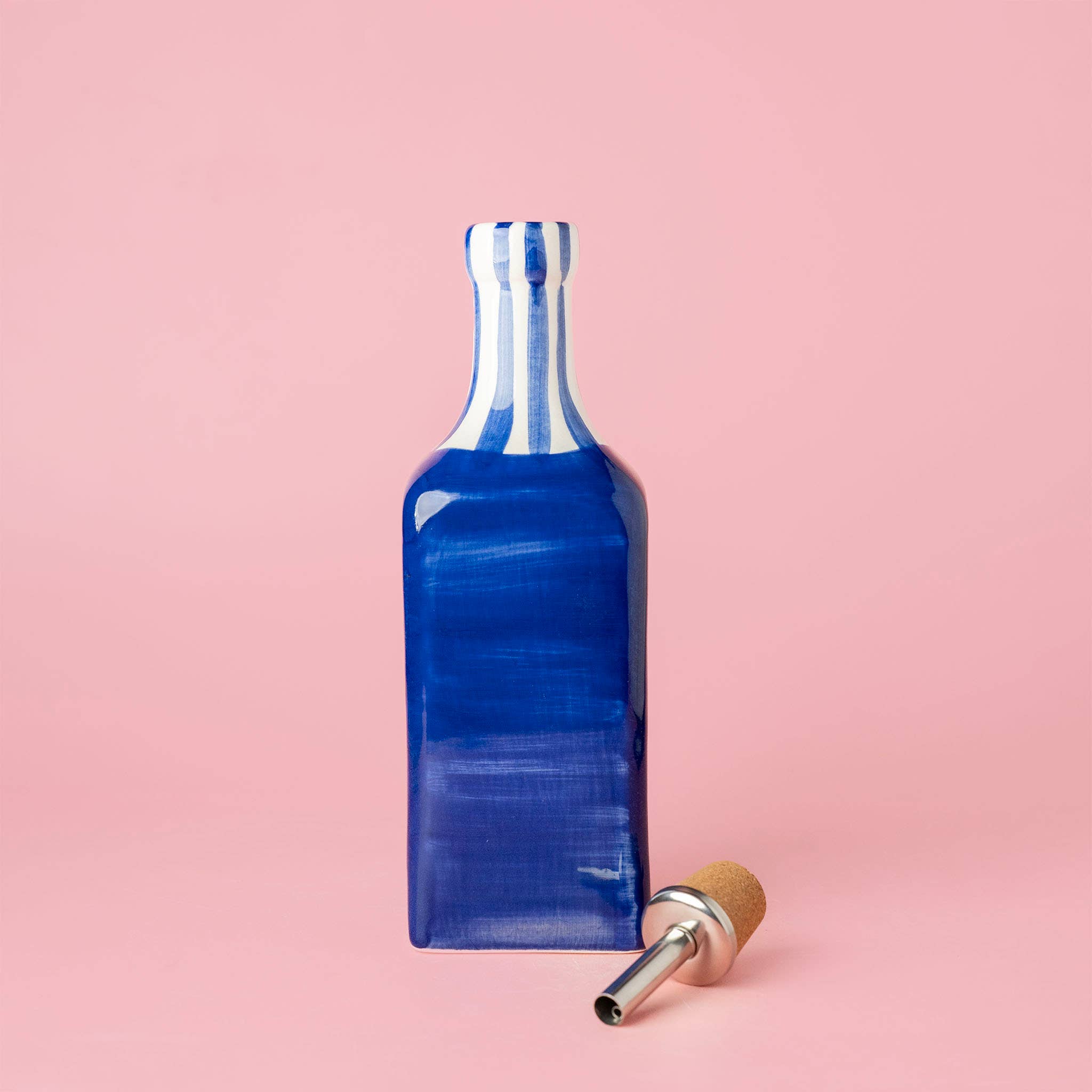 Blue ceramic oil pourer with a cork stopper on a pink background