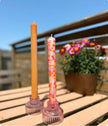 Two candles on pink holders with a blurred outdoor background