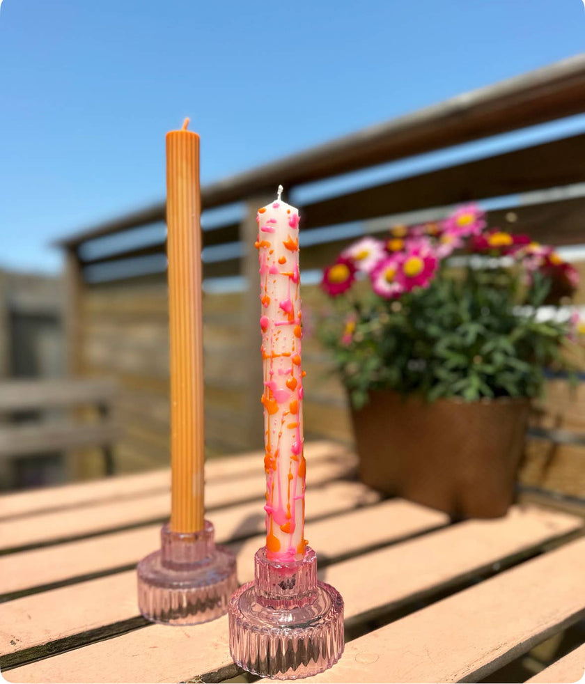 Two candles on pink holders with a blurred outdoor background