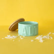 Green salt container with wooden lid on a yellow background