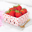 Pink ceramic basket with red heart patterns filled with strawberries on a white background
