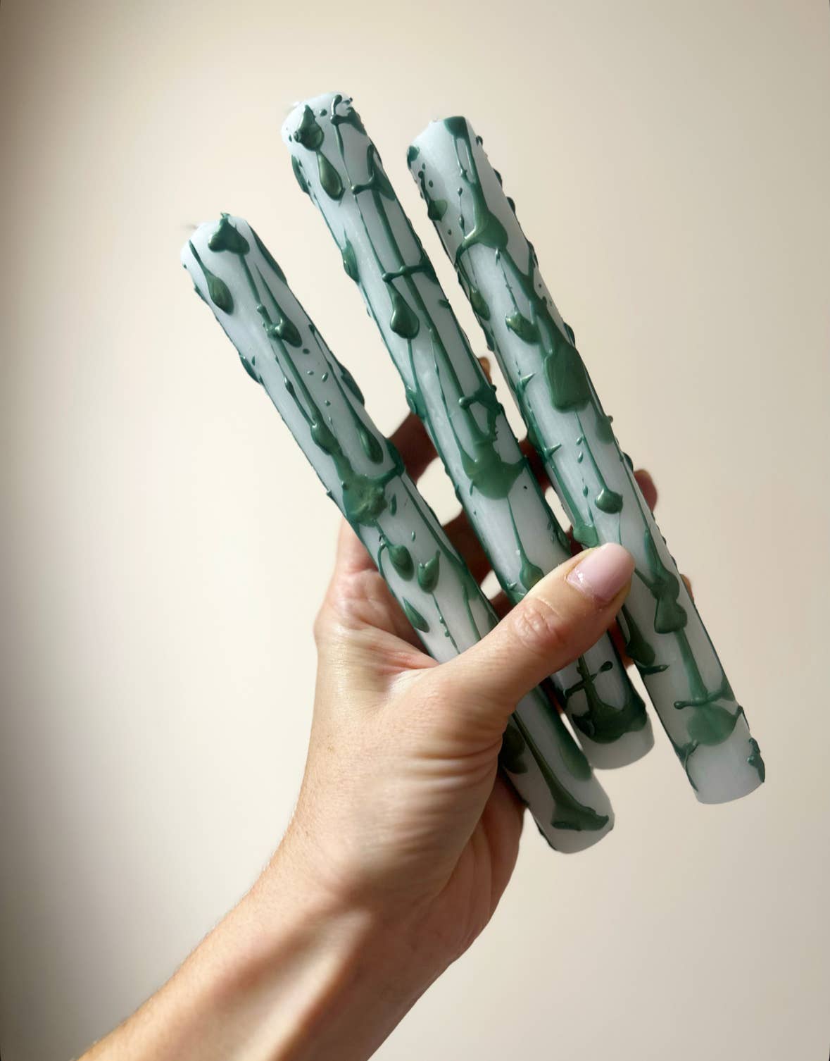 Hand holding three candles with green and white splash designs against a plain background