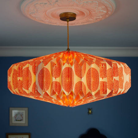 Decorative ceiling paper lightshade with orange patterned shade against a blue wall.