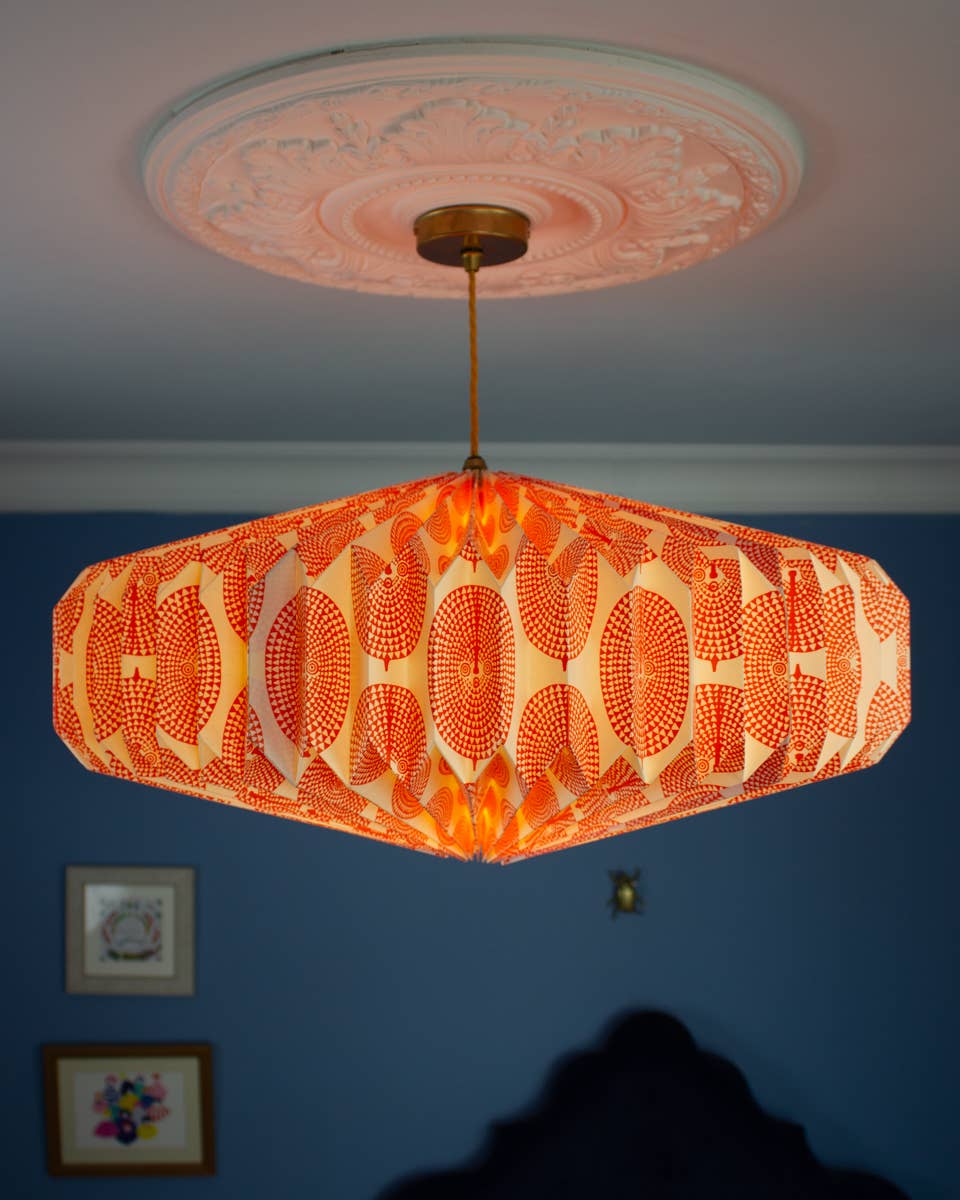 Decorative ceiling paper lightshade with orange patterned shade against a blue wall.
