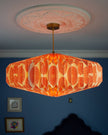 Decorative ceiling paper lightshade with orange patterned shade against a blue wall.