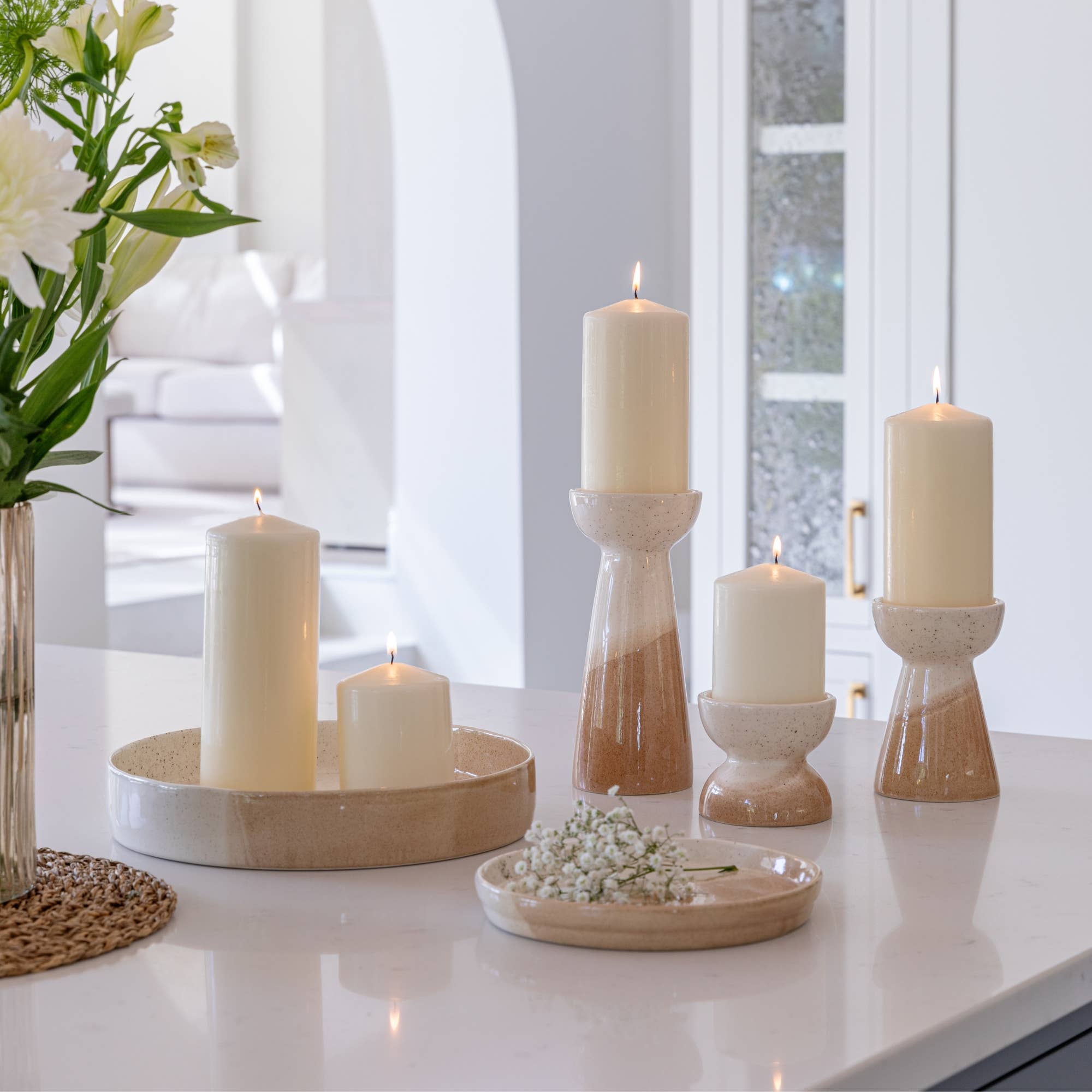 Decorative candles and flower arrangement on a white surface with a blurred background