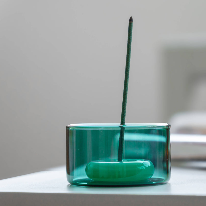 Green incense stick in a glass container on a light surface with a blurred background